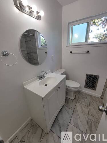 A bathroom with a sink, mirror, toilet, and a window.