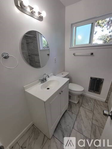 A bathroom with a sink, mirror, toilet, and a window.