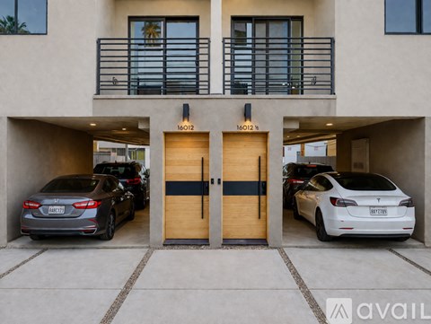 Two cars are parked in front of a building with two doors.