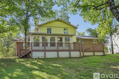 A yellow house with a deck and a tree in front.
