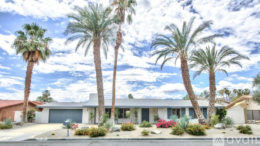 A house with a red roof and a white garage door is surrounded by palm trees.