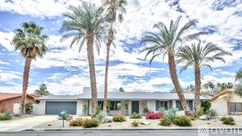 A house with a red roof and a white garage door is surrounded by palm trees.