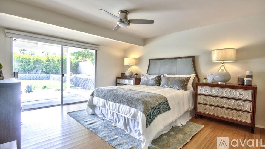 A bedroom with a large bed, a ceiling fan, and a sliding glass door leading to a patio.