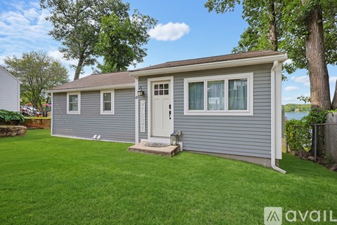 A grey house with a white door and windows is surrounded by a green lawn.