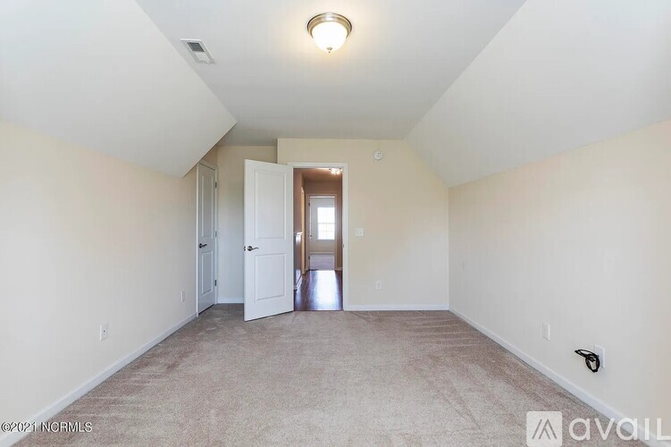 A spacious room with beige carpeting and white walls, featuring a doorway leading to another room.