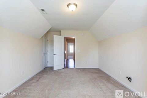 A spacious room with beige carpeting and white walls, featuring a doorway leading to another room.
