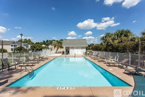 A large swimming pool surrounded by a fence and lounge chairs.
