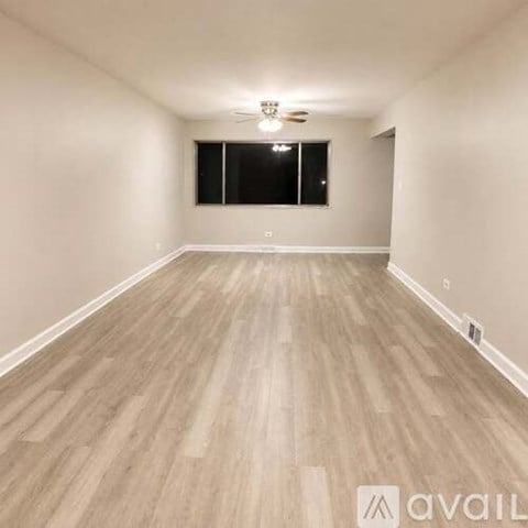 A spacious room with wooden flooring and a window with black blinds.