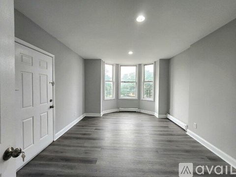 A spacious room with a white door and a window with a view of trees.