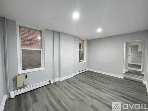 A room with grey flooring and a window showing a brick wall outside.