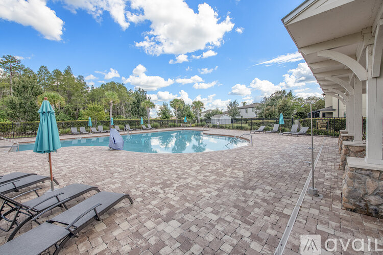 A pool area with a stone patio and a person sitting by the pool.