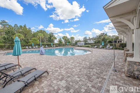 A pool area with a stone patio and a person sitting by the pool.