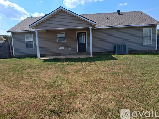 A house with a grey siding and a dark grey door is surrounded by a grassy area.