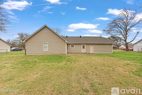 A house with a brown roof and a grey garage door is surrounded by a grassy field.
