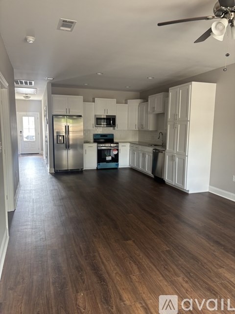 A spacious kitchen with white cabinets and a dark wood floor.