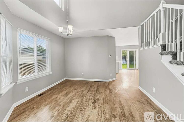 A spacious room with wooden flooring and a staircase on the right side.