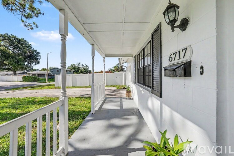 A white porch with a black lantern and the number 6717 on the wall.