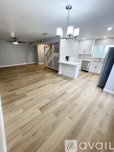 A spacious room with wooden flooring and a kitchen area in the background.