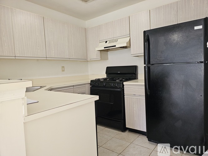 A black fridge stands in a kitchen with white cabinets and appliances.