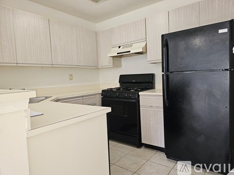 A black fridge stands in a kitchen with white cabinets and appliances.