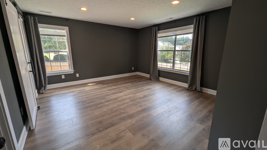 A spacious room with wooden flooring and large windows.