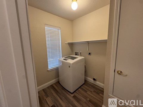 A small room with a washing machine and a window with blinds.