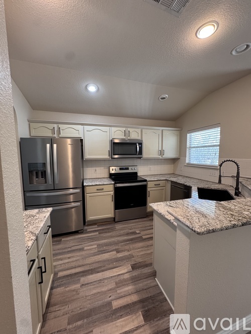 A kitchen with a refrigerator, microwave, oven, and sink.