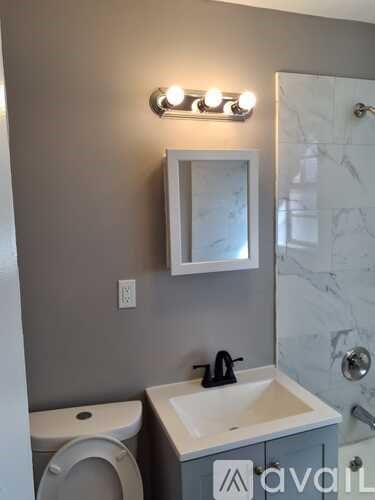 A bathroom with a toilet, sink, mirror, and lights.
