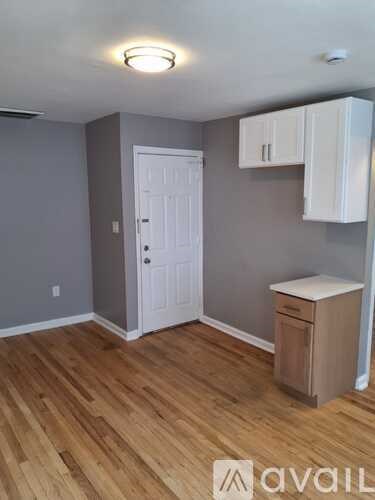 A room with a white door, wooden floors, and a trash can.
