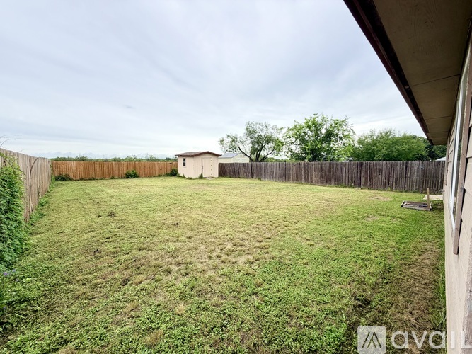 A backyard with a wooden fence and a small building in the distance.