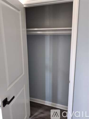 A white door with a black handle is open to a room with a grey wall.