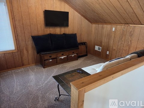 A living room with a black couch and a television mounted on the wall.