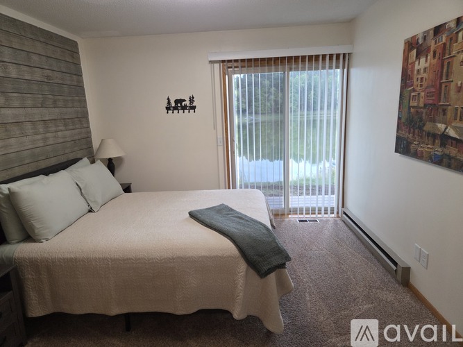 A bedroom with a bed, a lamp, a window with blinds, a carpet, and a painting on the wall.