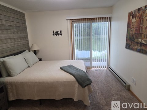 A bedroom with a bed, a lamp, a window with blinds, a carpet, and a painting on the wall.