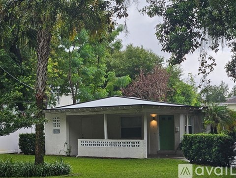 A house with a green door and a white porch is surrounded by trees.