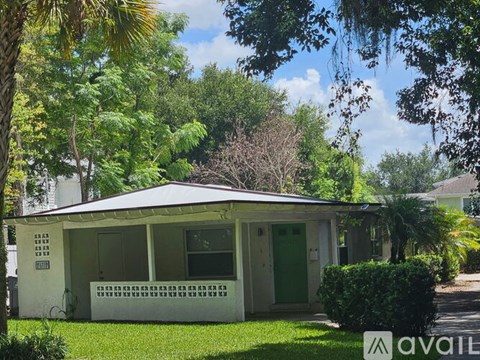 A house with a green door is surrounded by trees and has a sign that says "available".