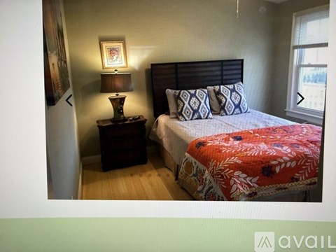 A bedroom with a bed, a nightstand with a lamp, and a window.