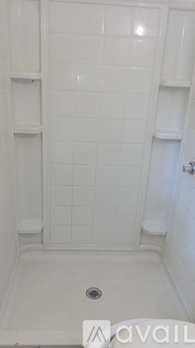 A white tiled shower stall with a drain in the middle.