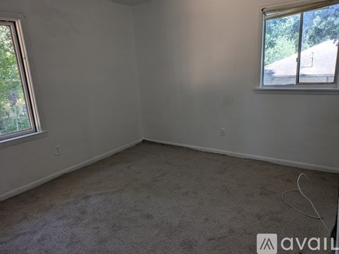 A room with a carpeted floor and two windows.