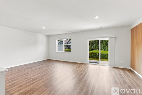 A spacious room with wooden flooring and a large window showing a view of a garden outside.