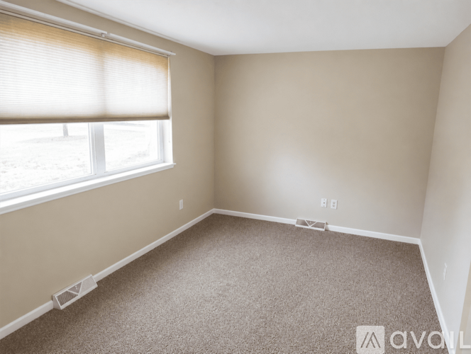 A room with a carpeted floor and a window with blinds.