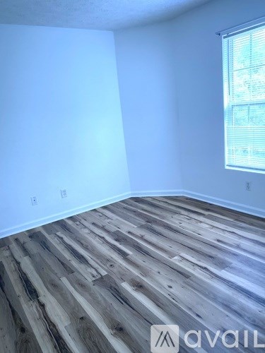 A room with wooden flooring and a window with blinds.