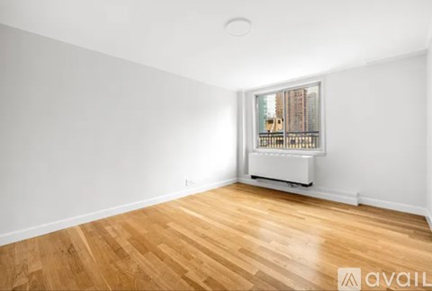 A room with wooden flooring and a window showing a city view.