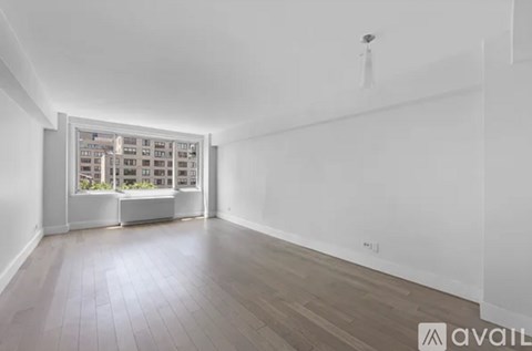 A spacious room with wooden flooring and a large window overlooking a building.