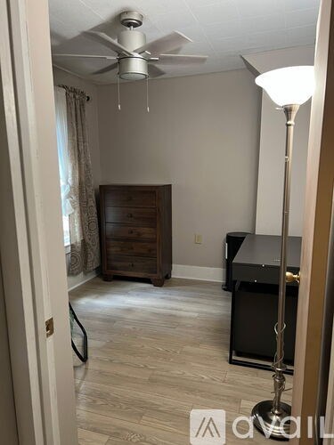 A room with a ceiling fan, a piano, and a lamp.