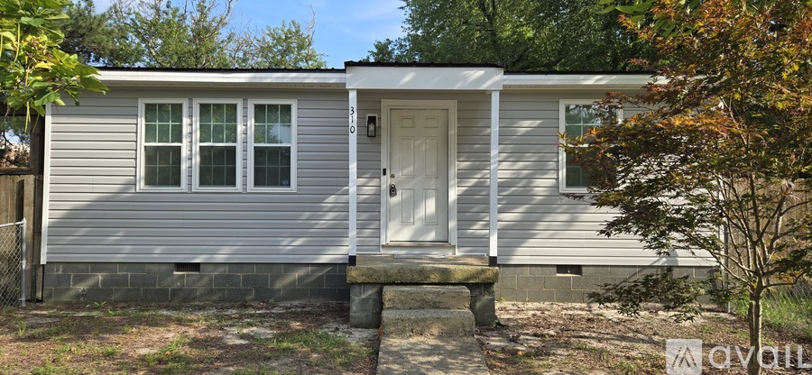 A small house with a white door and windows is surrounded by trees.