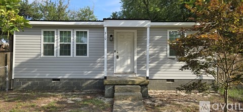 A small house with a white door and windows is surrounded by trees.