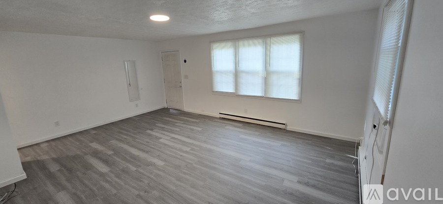 A spacious room with wooden flooring and a window with blinds.