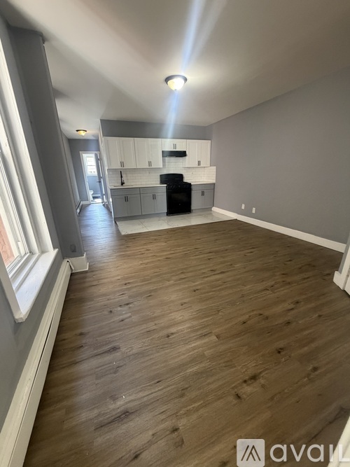 A spacious room with wooden flooring and a kitchen area in the background.