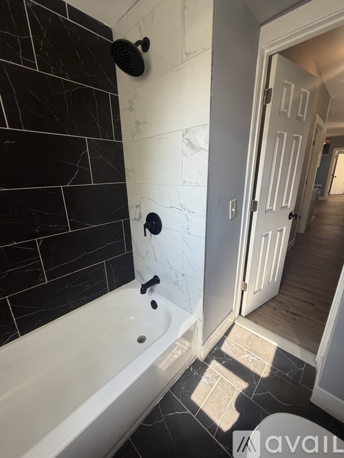 A bathroom with a black tiled shower area and a white bathtub.